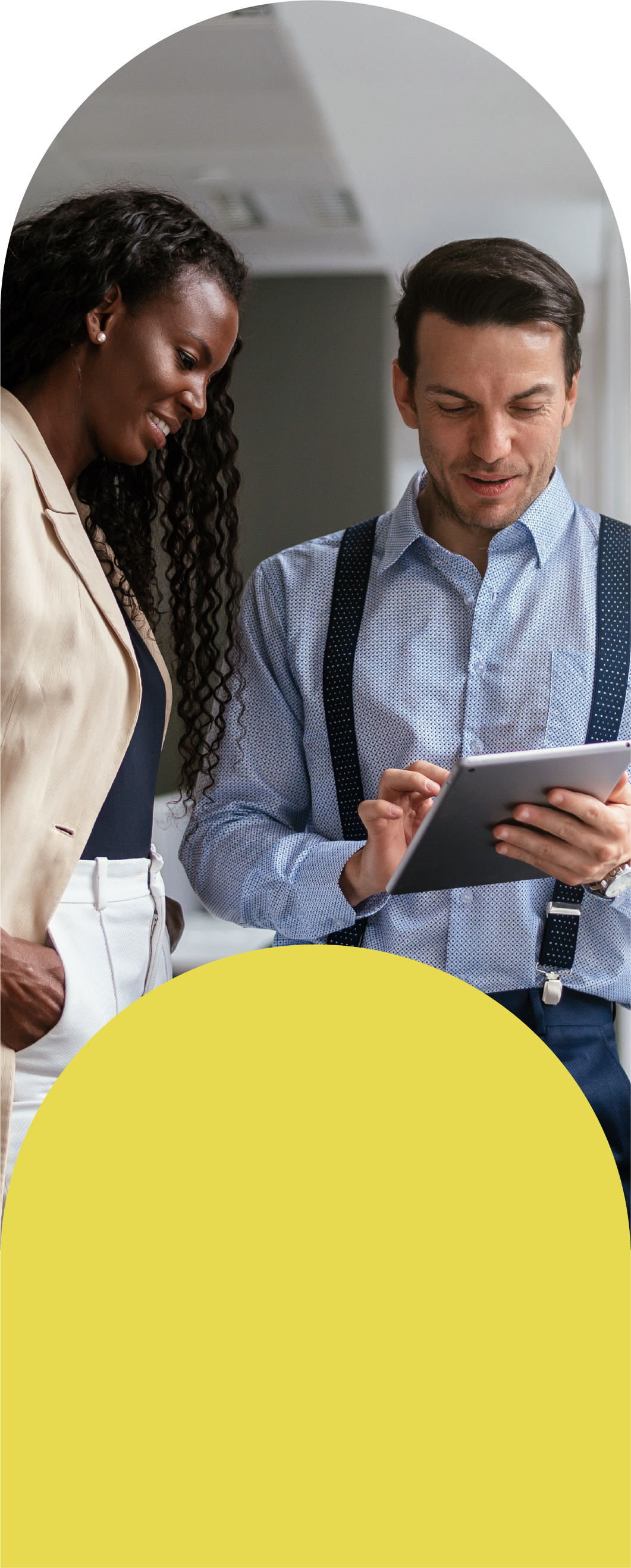 Two people discussing something while one holds a tablet and the other has hands in pockets.