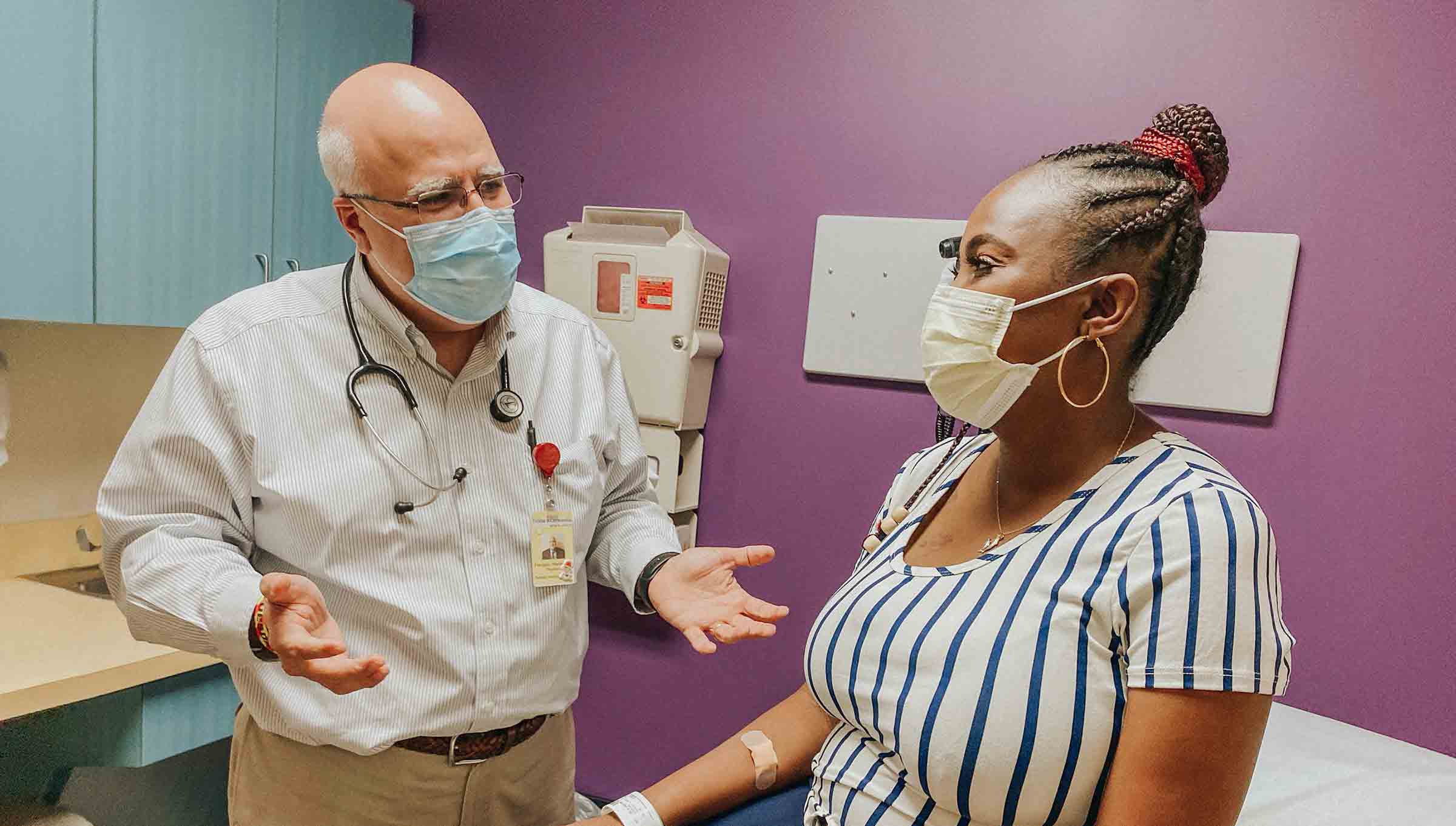 A doctor with a stethoscope discusses with a patient sitting on an examination table in a medical office.