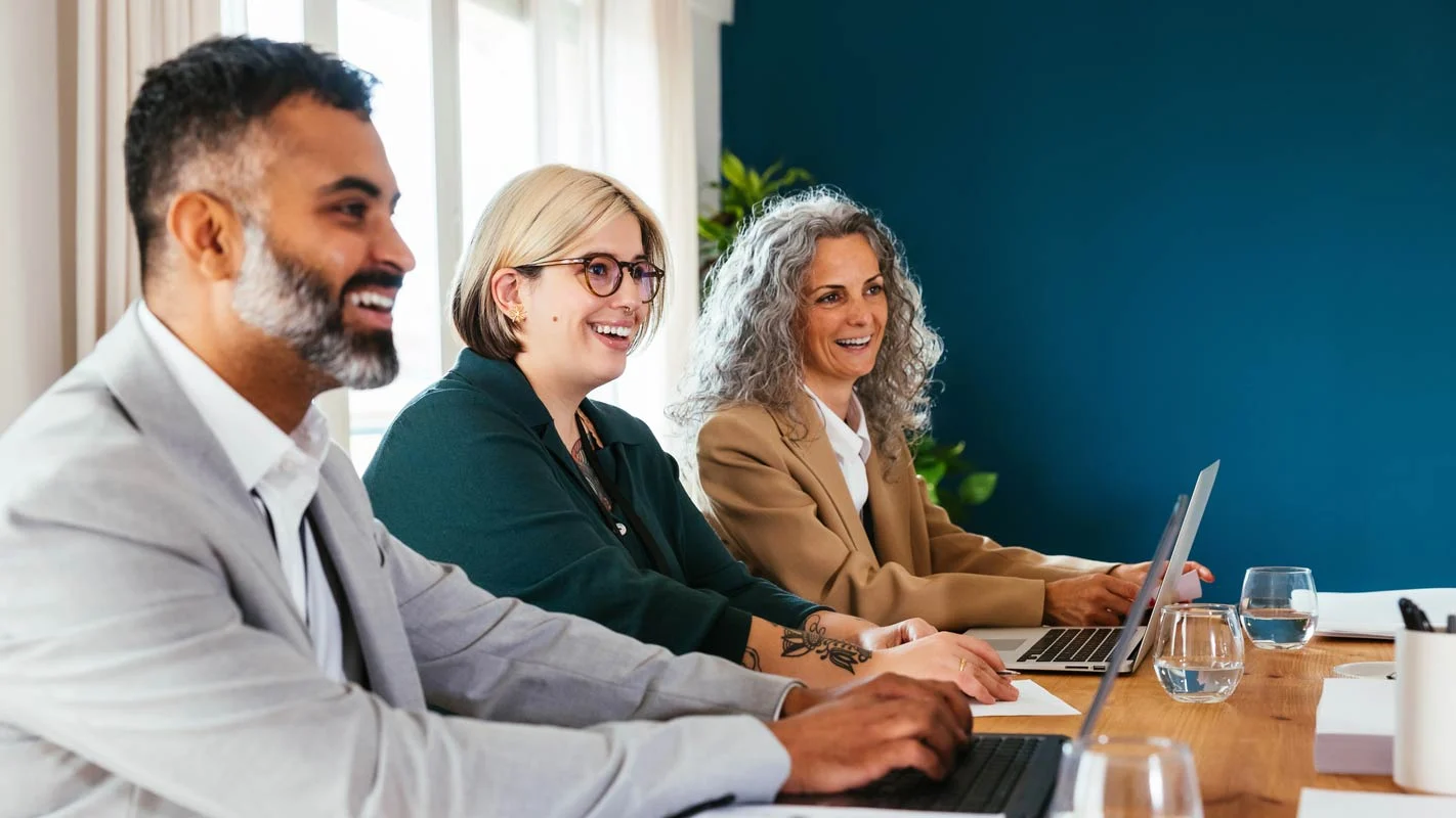 men and women colleagues sitting in a meeting room smiling