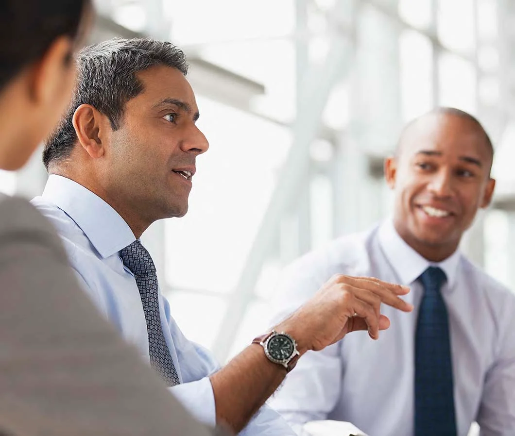 Three people in business attire are having a discussion in a well-lit office.