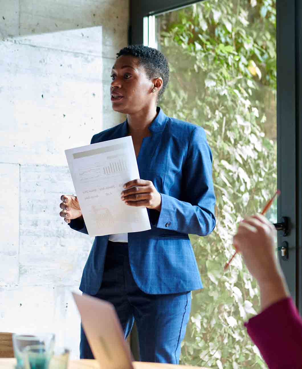 A person in a blue suit holds a document with charts in an office setting.