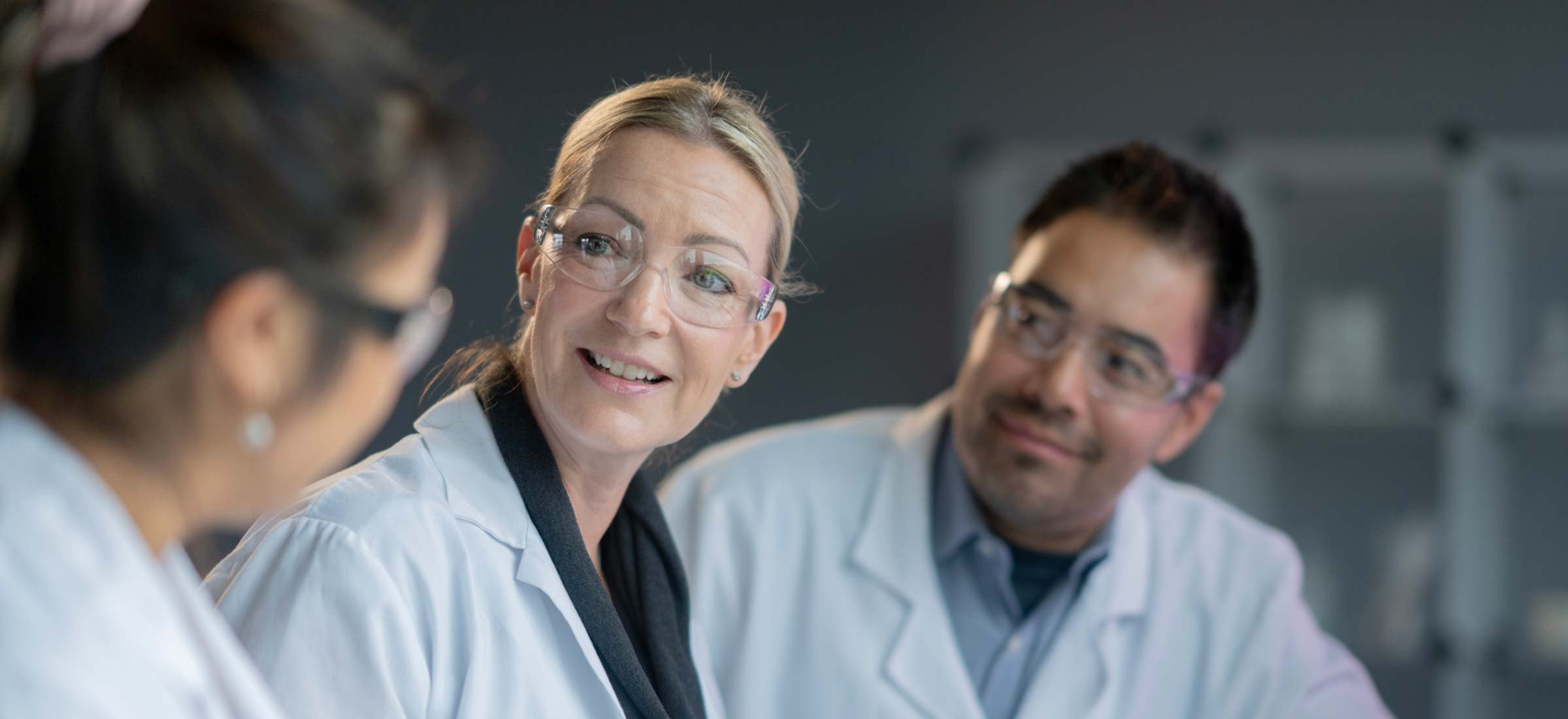 Group of people in lab coats having a discussion in a laboratory setting.