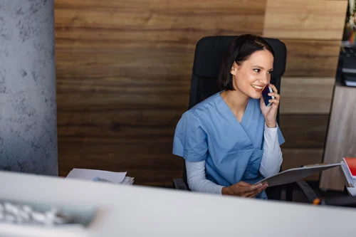 Nurse speaking on the phone while sitting at a desk and holding a chart